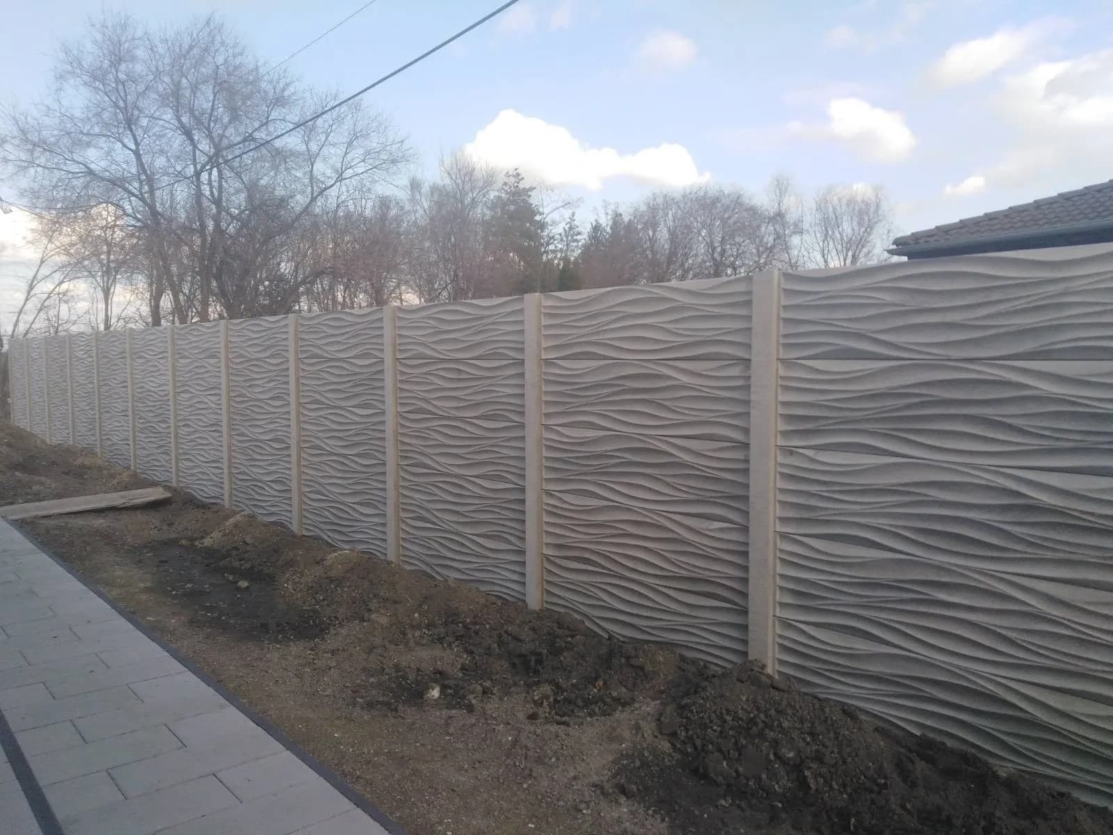 Hosszú, hullám mintás betonkerítés járda mellett