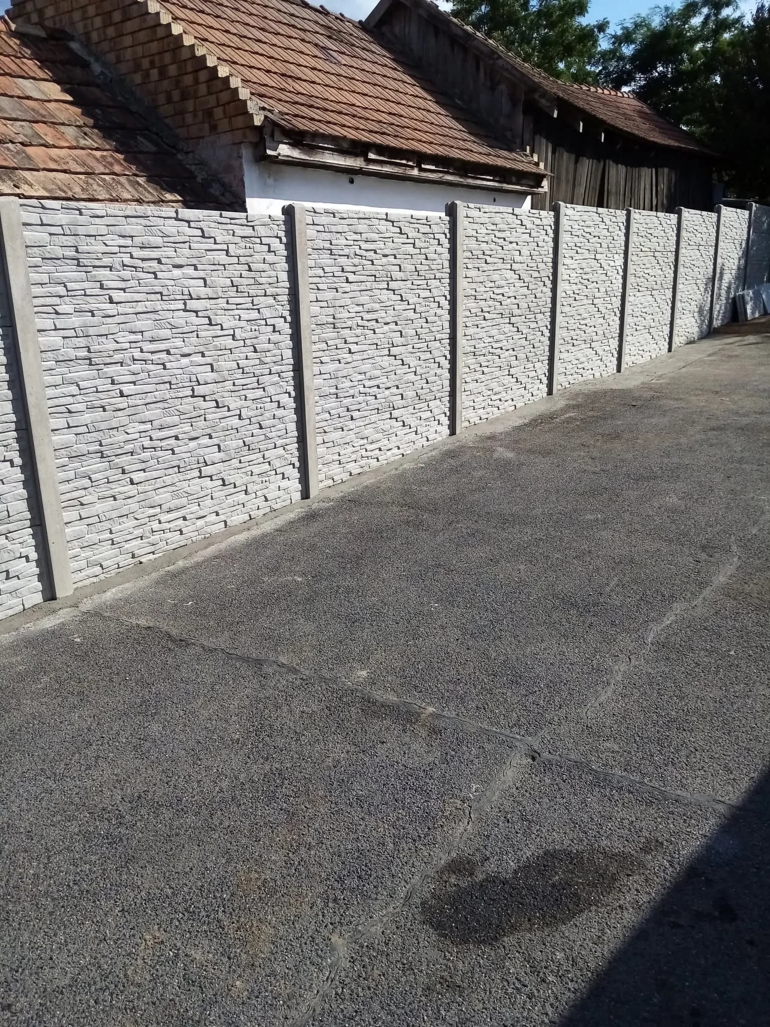 Szürke kőmintás kerítés egy lejtős kocsibejáró mentén