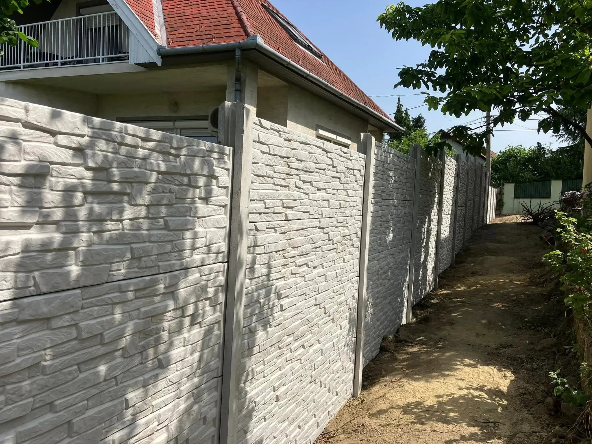 Fehér, szeletelt kő mintás elemes betonkerítés egy családi ház mellett